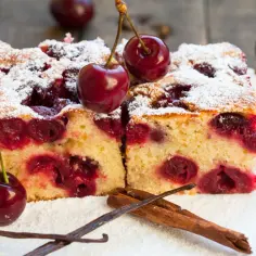 Dwa kawałki ciasta z czereśniami, posypane cukrem pudrem, z wisienkami na wierzchu. To prawdziwe ciasto z czereśniami - niebo w ustach!