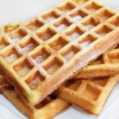 Stos świeżo upieczonych gofrów, posypanych cukrem pudrem. Idealne na najprostszy przepis na gofry.