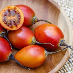 Kilka dojrzałych tamarillo w drewnianej misce. Jedno przekrojone ukazuje galaretowaty miąższ z nasionami. Dowiedz się, jak jeść tamarillo!