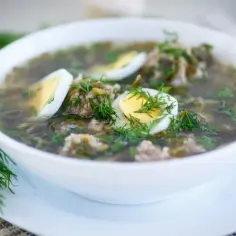 Zupa szczawiowa przepis babci: aromatyczna, zielona z dodatkiem mięsa i jajka, udekorowana świeżym koperkiem.