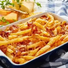 Zapiekane frytki z serem i chrupiącym boczkiem, podane w niebieskiej brytfance. Pyszne frytki z serem kuszą apetycznym wyglądem.