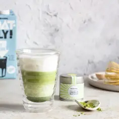 Warstwowy napój matcha z pianką, obok puszka z matchą i bambusowa miotełka. Idealny przepis, jak zrobic matche.