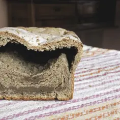 Chleb z zakalcem, z dziurą w środku, leży na kolorowym obrusie.