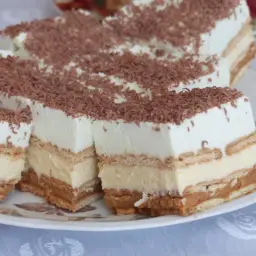 Szybkie ciasto bez pieczenia z budyniem i herbatnikami, udekorowane wiórkami czekolady. Idealne na deser!