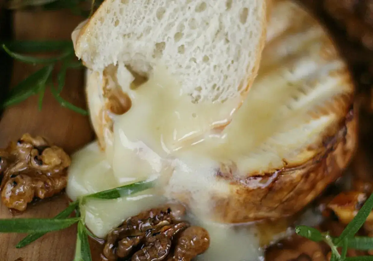 Pyszny, roztopiony pieczony camembert z chrupiącą skórką, podany z kawałkiem bagietki, orzechami i rozmarynem.
