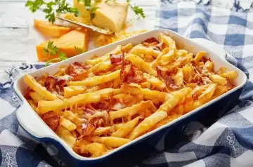 Zapiekane frytki z serem i chrupiącym boczkiem, podane w niebieskiej brytfance. Pyszne frytki z serem kuszą apetycznym wyglądem.