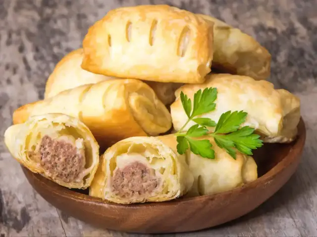 Stos pieczonego ciasta francuskiego z kiełbasą w środku, ozdobione natką pietruszki. Idealne na szybką przekąskę.